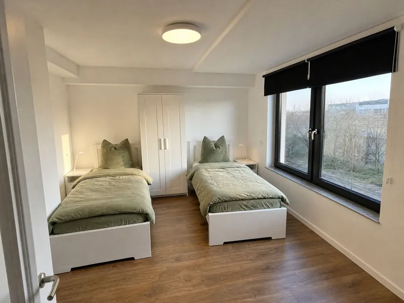 Zweibettzimmer mit grünen Tagesdecken und breiter Fensterfront