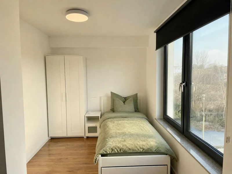 Einzelzimmer mit Bett, Kleiderschrank und Fenster