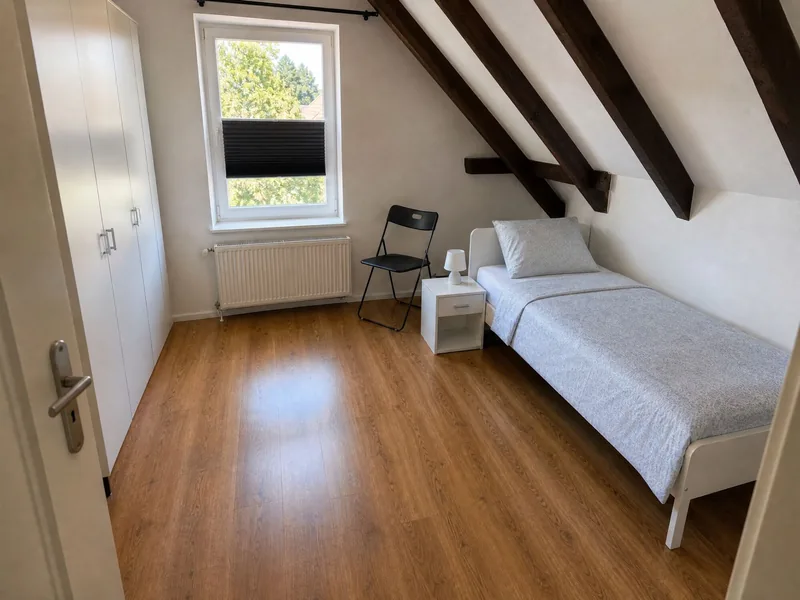 Einzelzimmer mit Bett, Stuhl und Fenster unter der Dachschräge