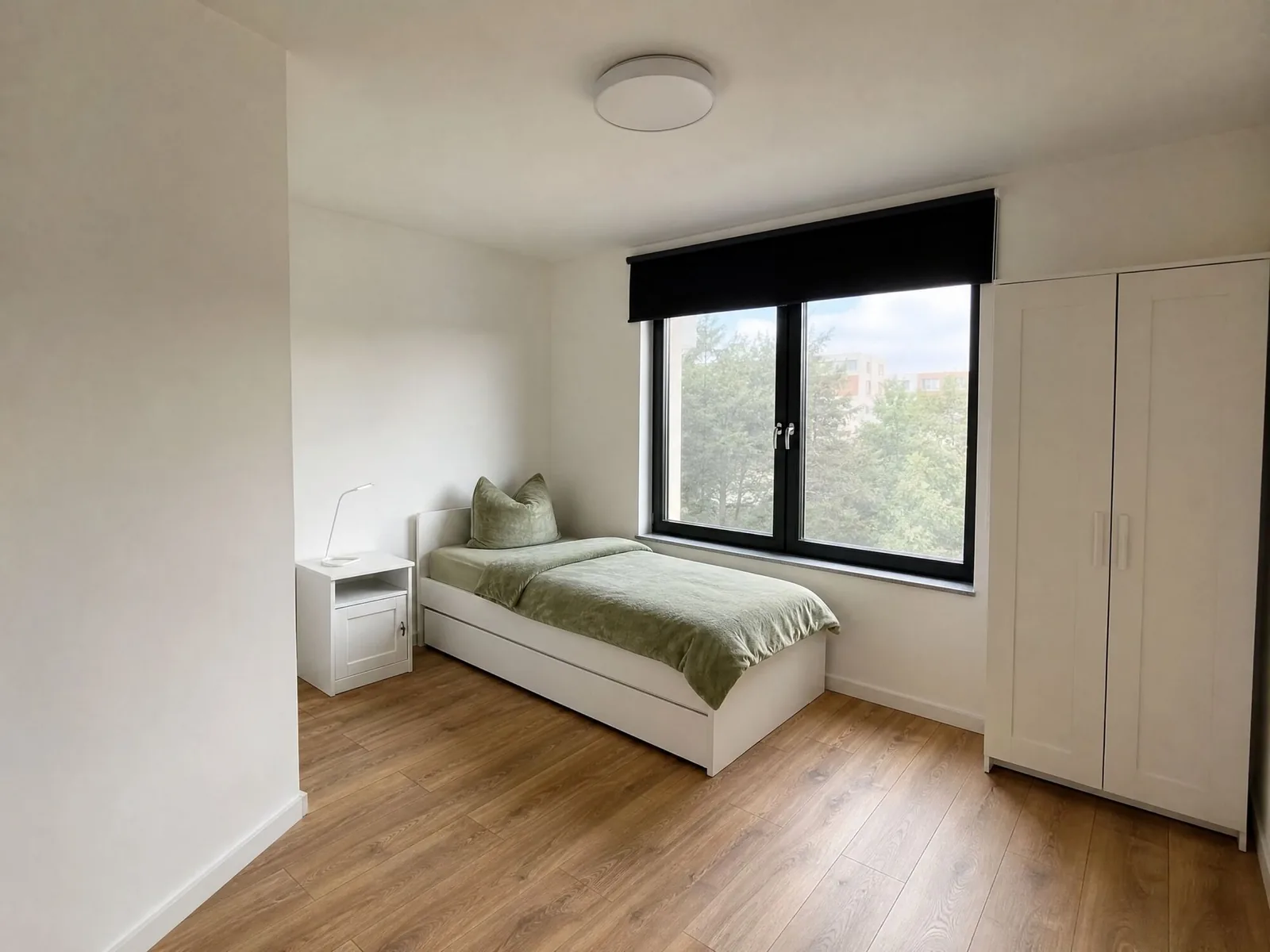 Einzelzimmer mit Bett am Fenster und Kleiderschrank